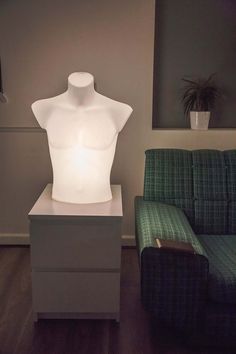 a white mannequin lamp sitting on top of a table next to a green couch