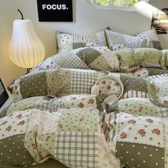 a bed covered in lots of pillows next to a night stand with a lamp on it