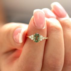 a woman's hand holding a ring with a green stone