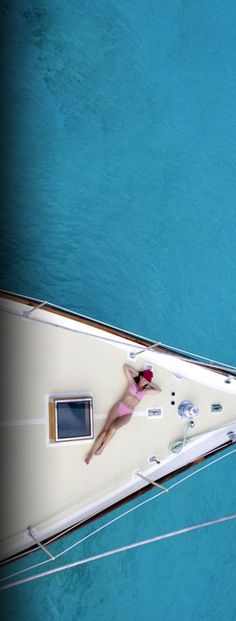 a woman laying on the bow of a boat in clear blue water, from above