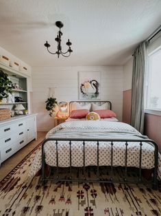 a bed sitting in a bedroom next to a window with a lamp on top of it