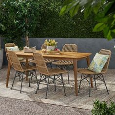 a wooden table with chairs around it in the middle of a patio area surrounded by greenery