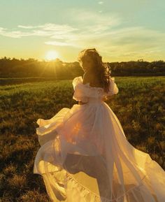 a woman in a white dress is standing in the grass at sunset with her hair blowing in the wind