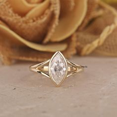 a gold ring with a pear shaped diamond on it and a rose in the background