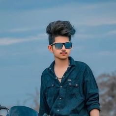 a young man wearing sunglasses standing next to a motorcycle