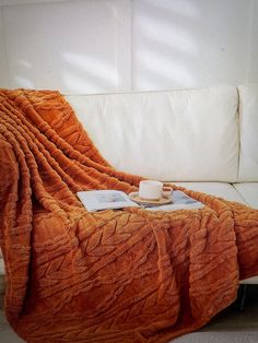 an orange blanket sitting on top of a couch next to a cup and saucer