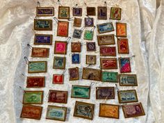 an assortment of framed stamps are displayed on a white cloth covered tablecloth with lace