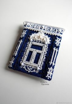 a blue and white beaded brooch sitting on top of a white table next to a cell phone