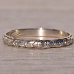 an antique wedding band with flowers and leaves engraved on the side, sitting on a wooden surface