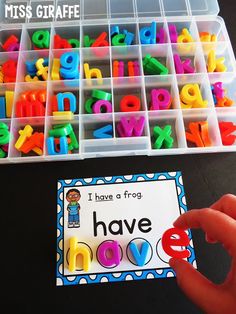 a hand holding a plastic container filled with letters and magnets next to a box full of letter magnets