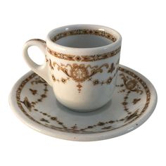 a white cup and saucer with gold designs on the rim, sitting on a plate