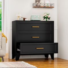 a black dresser with gold handles in a white living room next to a beige chair