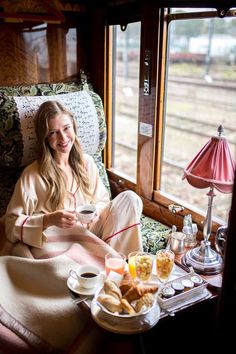 a woman sitting in a train car with food and drinks on the table next to her