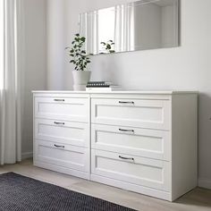 a white dresser sitting in front of a window next to a potted plant on top of a table