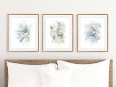 three framed pictures hang above a bed with white sheets, pillows and throw pillows on it