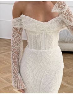 a woman wearing a white dress with long sleeves and an off the shoulder design on it