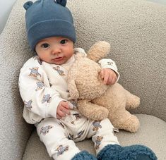 a baby sitting on a couch holding a teddy bear