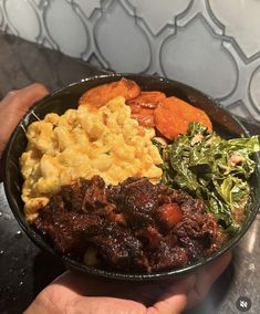 a person holding a bowl filled with food on top of a metal counter next to a tiled wall