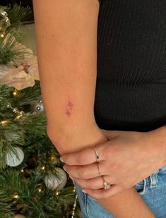 a woman wearing a black shirt and blue jeans is holding her hand in front of a christmas tree