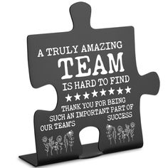 a black puzzle piece with the words team on it and flowers in white lettering that says,