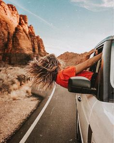 a woman leaning out the window of a car on a desert road with mountains in the background