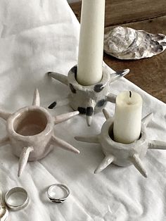 two white candles are sitting on a table with other silver rings and ring holders in front of them