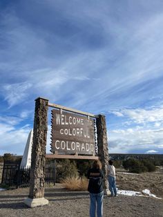 two people are standing in front of a welcome sign for the colorado national park on a sunny day