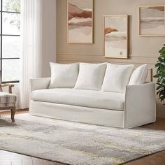 a living room with white furniture and paintings on the wall, rugs and windows