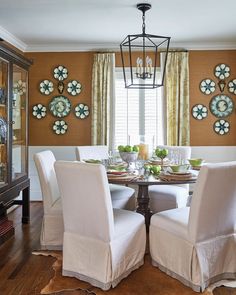 a dining room table with white chairs and plates on the wall