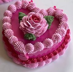 a heart shaped cake decorated with pink icing and flowers on top, sitting on a table