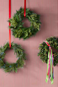 three christmas wreaths hanging from red and white striped wall with ribbons on them,