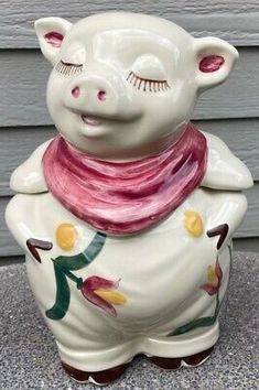 a ceramic pig with a scarf on it's neck sitting on the ground in front of a house