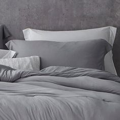 an unmade bed with grey sheets and pillows