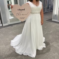 a woman in a white dress holding up a heart shaped sign