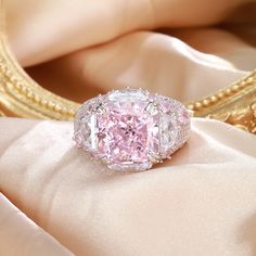 a fancy pink diamond ring sitting on top of a white satin covered table next to a gold framed mirror