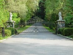 an iron gate with statues on each side in front of trees and bushes surrounding it