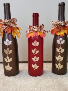 three wine bottles decorated with fall leaves and bows are sitting on the floor next to each other