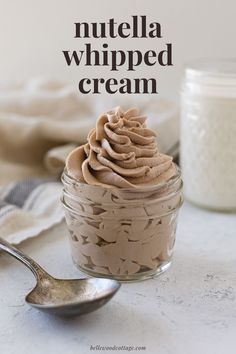 a glass jar filled with nutella whipped cream next to a spoon on a table