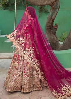 a woman in a red and gold bridal gown standing next to a tree branch