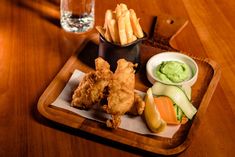 a wooden tray topped with different types of food next to a glass of water on top of a table