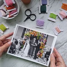 two hands holding up an old photo with yarn and scissors on the table next to it