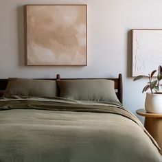 a bed with two paintings on the wall above it and a plant next to it