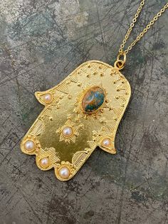 Hamsa Hand is very meaningful in many traditions. It's believed keep away from bad luck and negative things then turn them to Positive energy!! 21 ct gold plated brass. Turquoise and Pearl Length - Approx 83cm / top 6,5 x 5 cm Designed by our Turkish designer. Handcrafted with great care. Artisan Necklaces For Festivals, Traditional Turquoise Jewelry For Gift, Bohemian Round Pendant Necklace For Blessing, Artisan Jewelry For Festivals Or Gifts, Artisan Jewelry For Festivals And Gifts, Handmade Turquoise Necklace With Round Gold Pendant, Bohemian Engraved Turquoise Necklaces, Handmade Gold Turquoise Necklace With Round Pendant, Handmade Spiritual Turquoise Necklace With Round Pendant