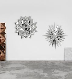 three metal sculptures are on the wall next to each other in an empty room with concrete flooring