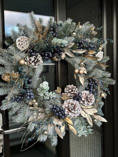 a wreath with pine cones, berries and evergreen leaves on it is hanging from the front door