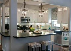 a kitchen with white cabinets and black counter tops, lights hanging from the ceiling over the island