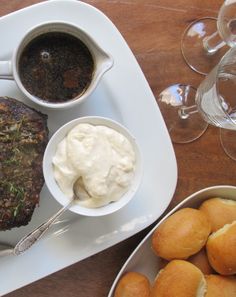 a plate with meat, potatoes and sauce on it next to some glasses of wine