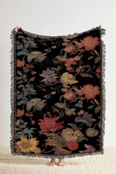 a black blanket with multicolored flowers and fringes hanging on a white wall