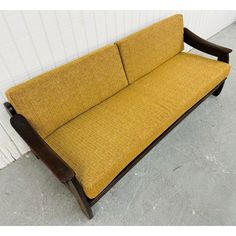 a yellow couch sitting on top of a cement floor next to a white brick wall