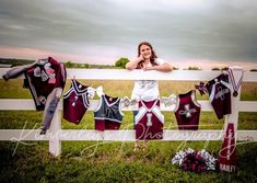 a woman leaning on a fence with her arms behind her head, surrounded by sports jerseys and wreaths